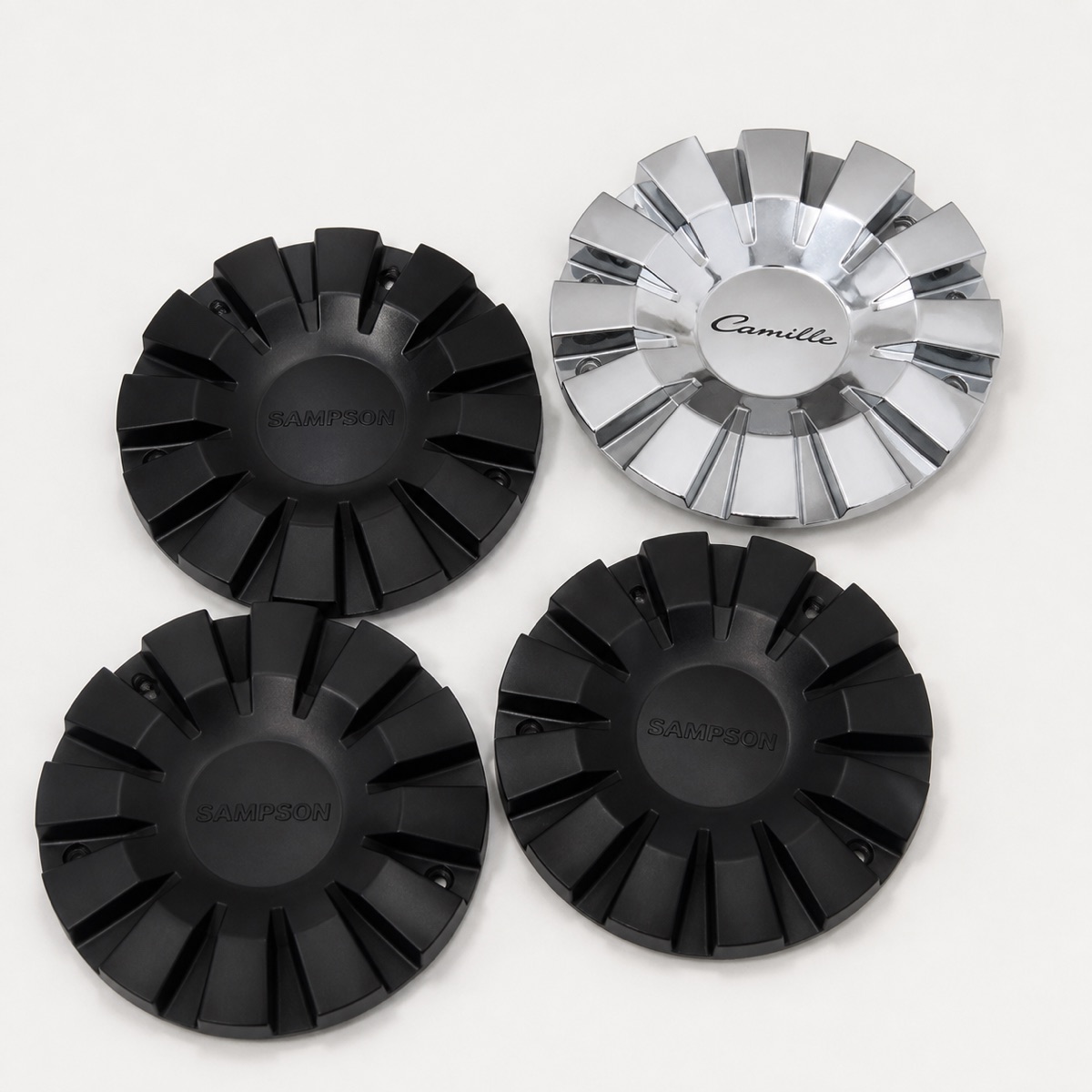 Three black 3D printed wheel center caps next to the original chrome cap